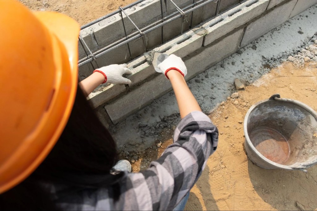 Worker laying concrete blocks with mortar and steel reinforcement for a residential foundation wall