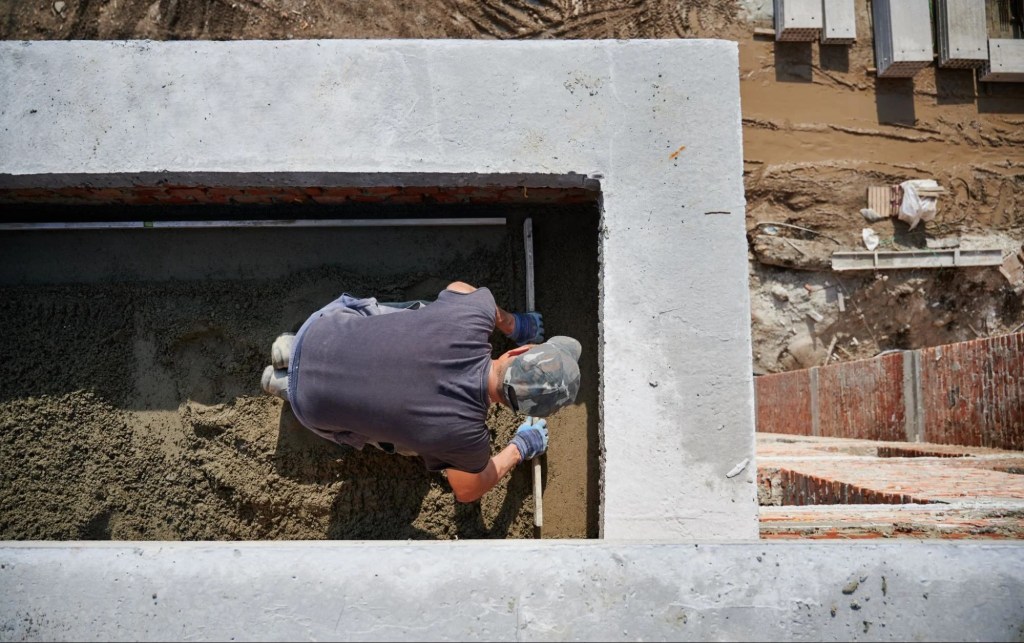 Worker placing and leveling fresh concrete inside a strip footing foundation trench at a residential construction site